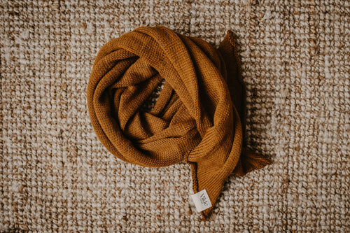 Ein Schal in der Farbe Kupfer-braun liegt auf einem beigen Hintergrund. Die Farbe ist intensiv und farbenfroh. Am Rand des Schals ist der Vilde Joranger Logo zu sehen. Die Etikette ist weiß mit schwarzem Schriftzug. 